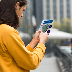 Person in yellow sweater uses a transparent smartphone outside near a building, symbolizing modern web design innovation.