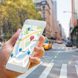 Person holding smartphone with a map of location markers, city buildings, and yellow taxis, suggesting local SEO opportunities.