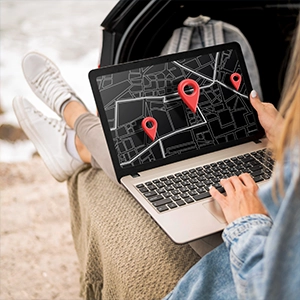 Person uses laptop showing map with red pins by an open car trunk, highlighting travel web design and SEO services.