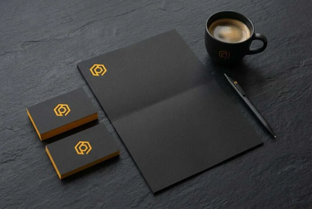 Black and amber branded stationery flat-lay with business cards, letterhead and a logo mark